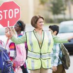 Photo of crossing guard holding stop sign with children passing by