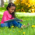 Photo of child reading book outdoors by tree