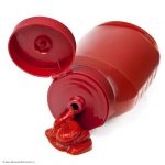 Photo of ketchup bottle on side with ketchup squeezed out from tip